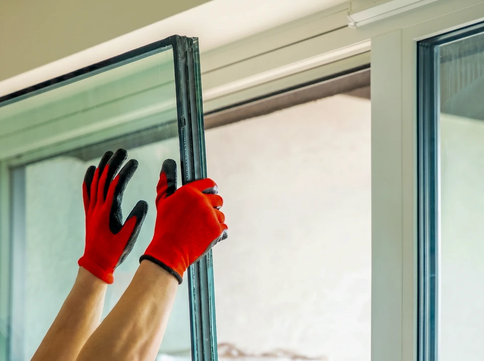 Un technicien en tenue professionnelle contrôle minutieusement le mécanisme de fermeture d'une porte d'entrée résidentielle, en examinant les joints et la charnière avec une précision méthodique, symbolisant l'inspection préventive rigoureuse.