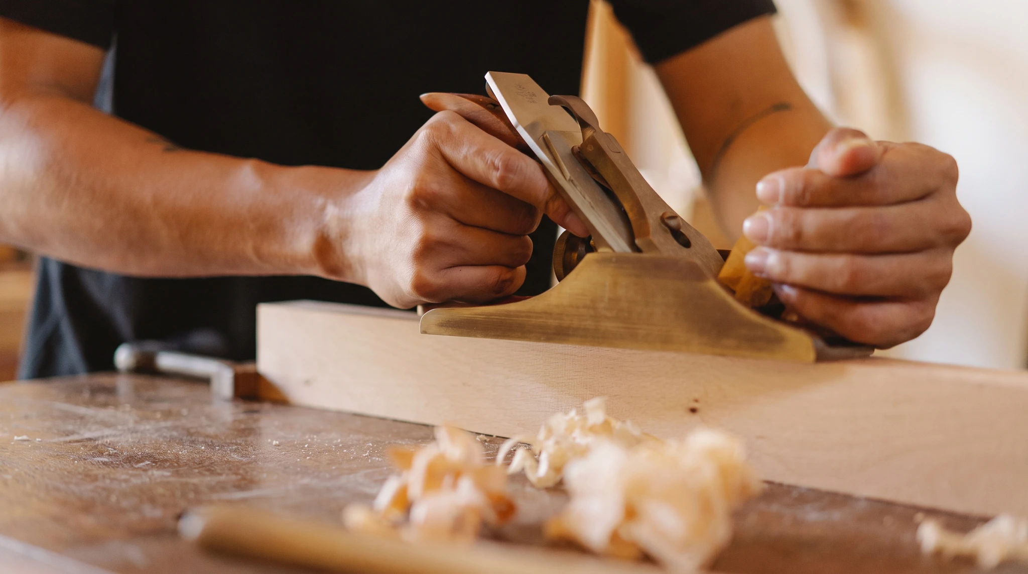 Artisan menuisier en tenue de travail, entrain de réparer ou régler le mécanisme d'un volet roulant blanc installé sur la façade en brique d'une maison individuelle, utilisant un tournevis ou autre outil de réparation.